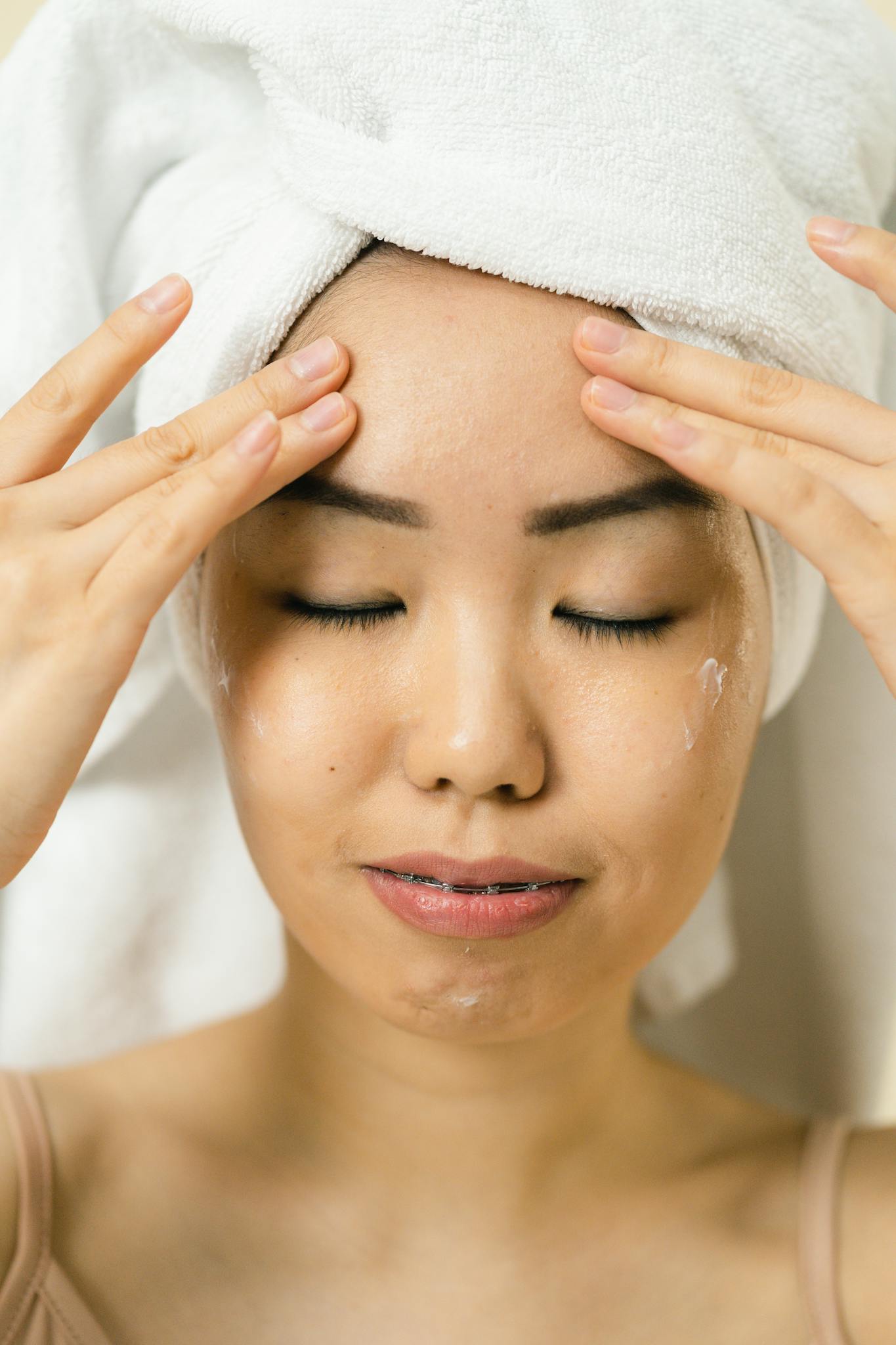 Portrait of a woman with a towel, eyes closed, experiencing relaxation during a spa facial treatment.