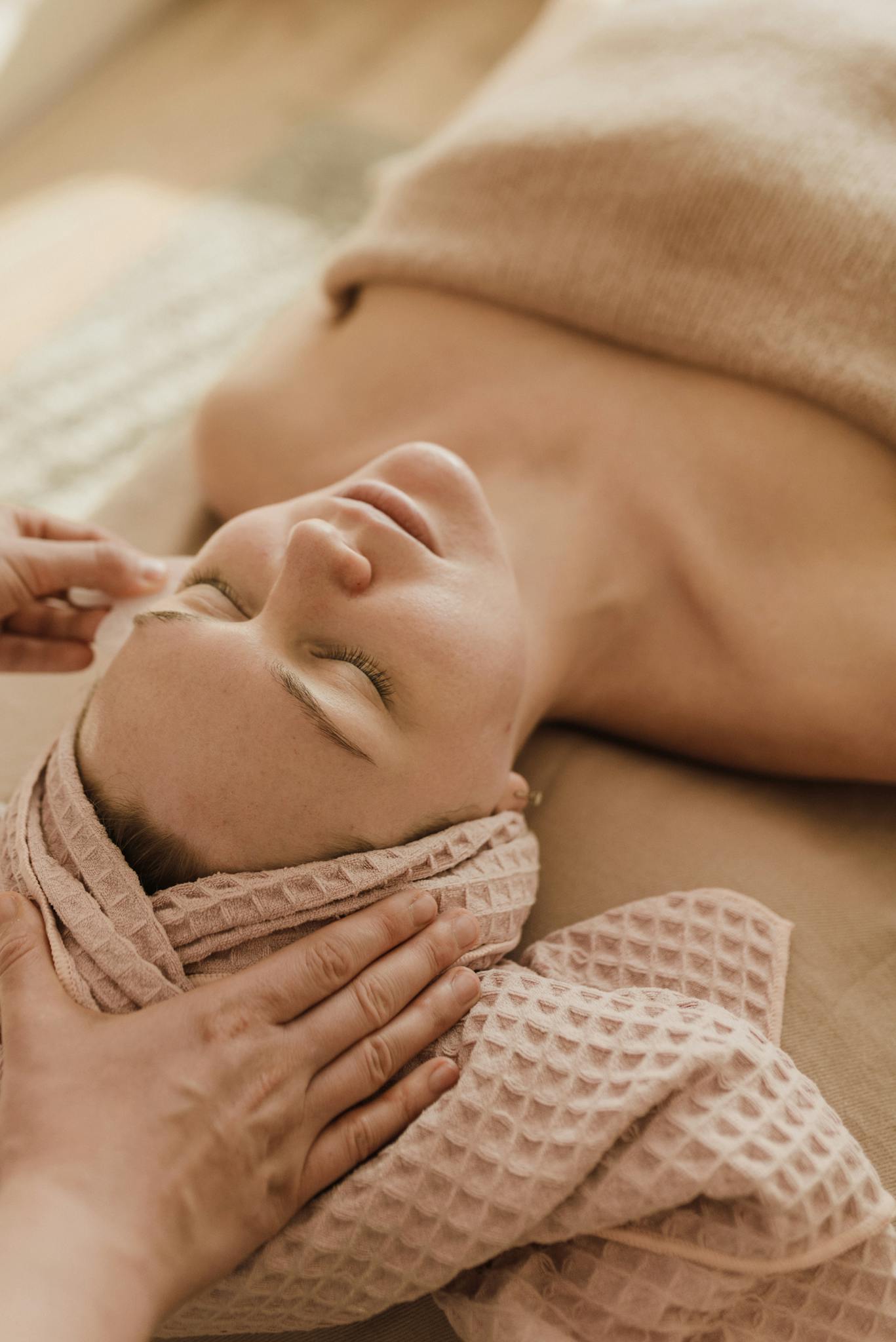 Woman enjoying a relaxing facial spa treatment with a towel wrap, eyes closed in serenity.